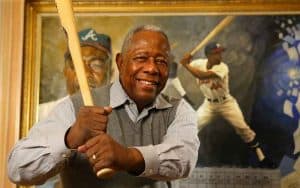 mlb home run king hank aaron posing with a bat in front of his portrait