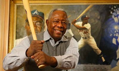 mlb home run king hank aaron posing with a bat in front of his portrait
