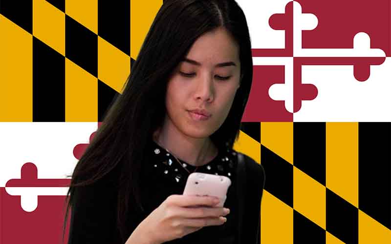 seorang wanita bertaruh pada olahraga di ponsel cerdasnya di depan bendera negara bagian Maryland