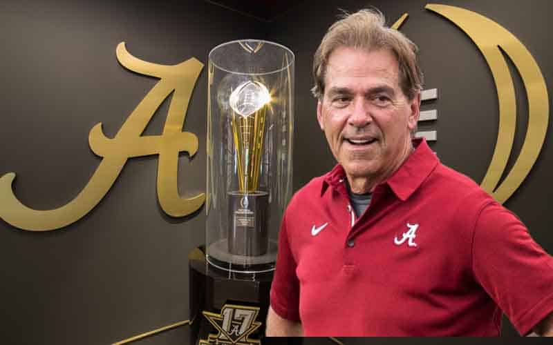 Nick Saban standing in front of an Alabama CFP National Championship Trophy