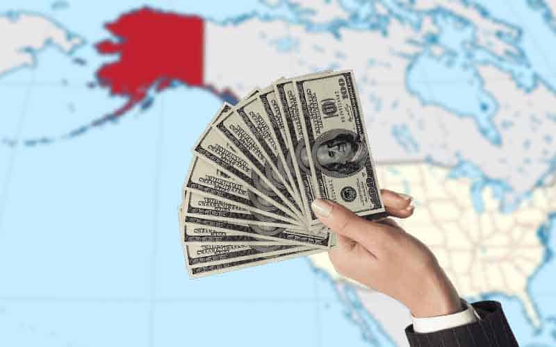 a hand offering money to Alaska on a map outlined in red