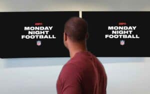 a man looking away from the camera at two tvs on the wall with Monday Night Football logos on them