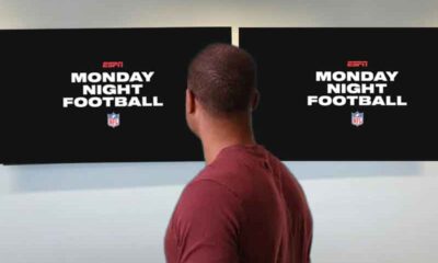 a man looking away from the camera at two tvs on the wall with Monday Night Football logos on them