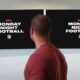 a man looking away from the camera at two tvs on the wall with Monday Night Football logos on them