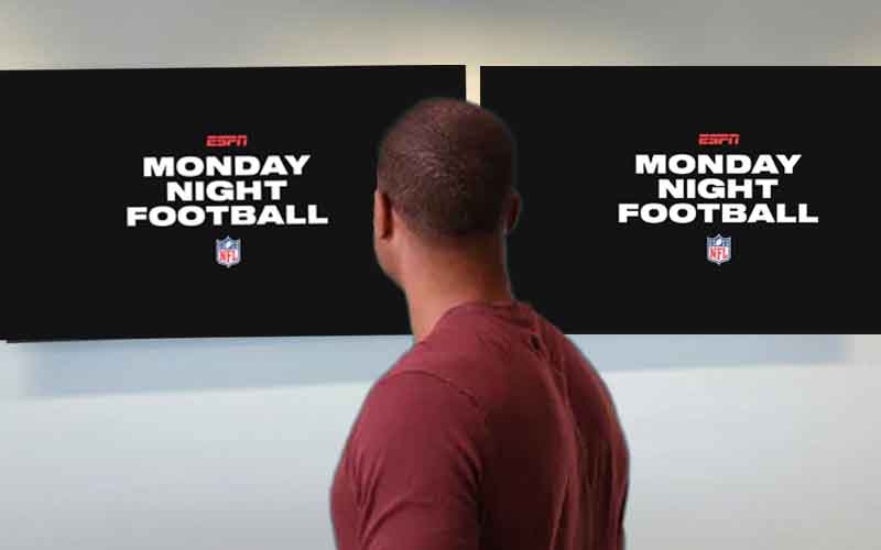 a man looking away from the camera at two tvs on the wall with Monday Night Football logos on them