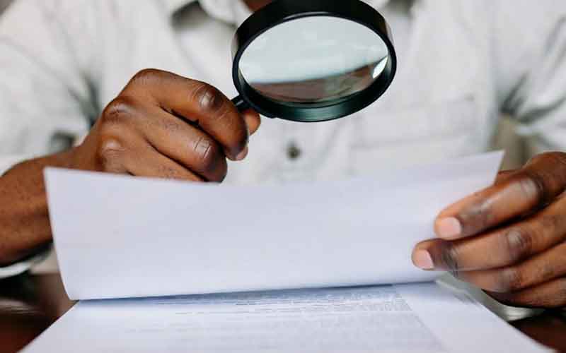 A man using a magifying glass to read sportsbook playthrough conditions