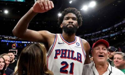 Philadelphia 76ers player in a white jersey with number 21 raises his fist amid cheering fans after a game.