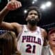 Philadelphia 76ers player in a white jersey with number 21 raises his fist amid cheering fans after a game.