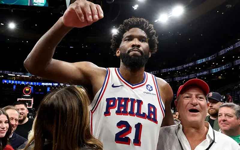 Philadelphia 76ers player in a white jersey with number 21 raises his fist amid cheering fans after a game.