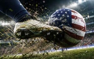 Soccer cleat kicking a muddy ball painted with the US flag on a stadium field.